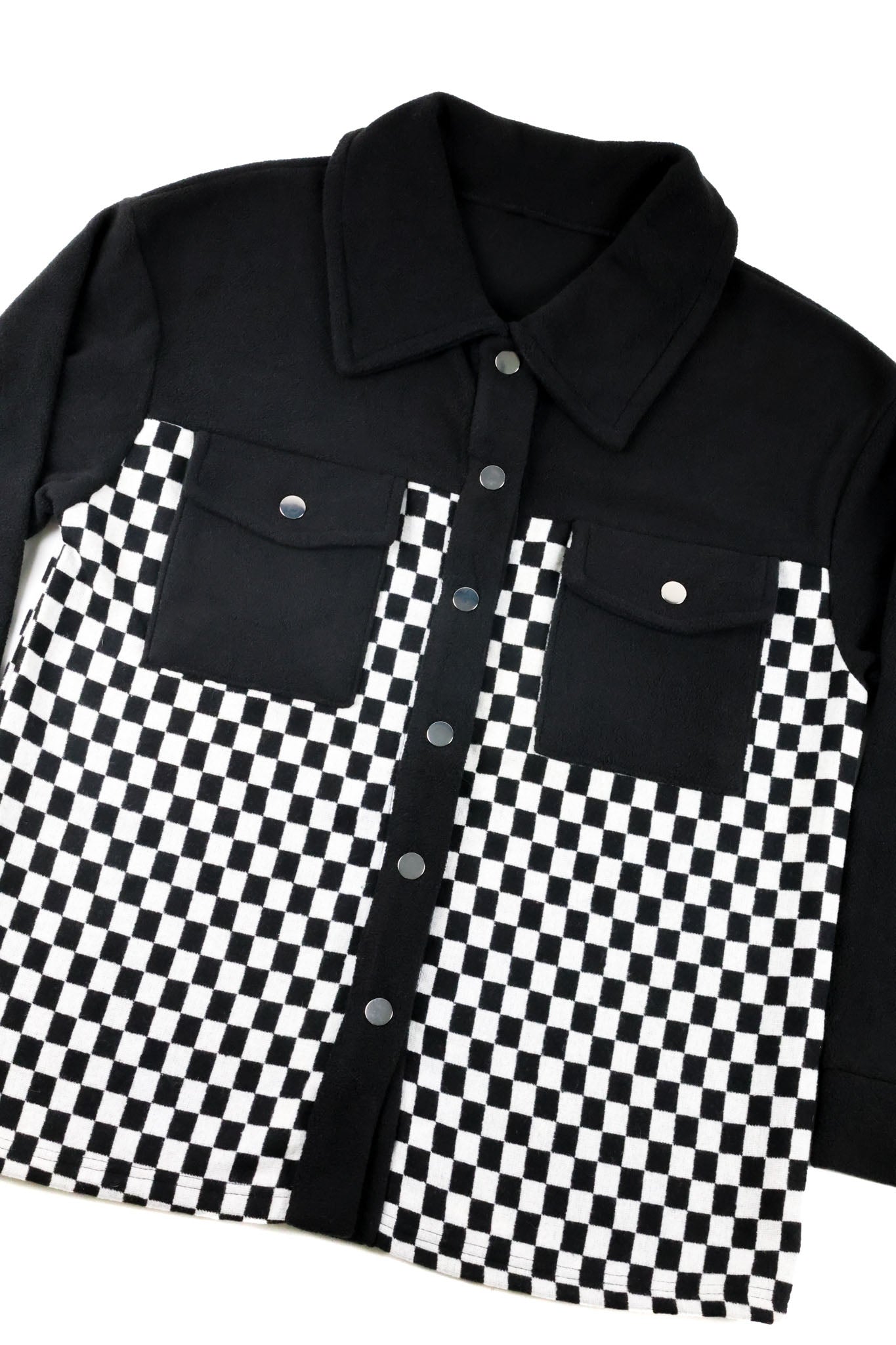 A long-sleeve button-up shirt jacket featuring a solid black upper portion and collar, with a black and white checkerboard patterned lower body and front panel.
