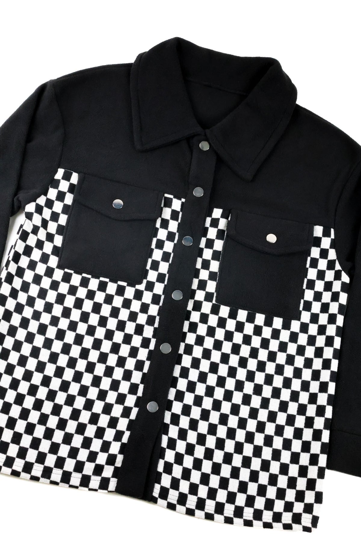 A long-sleeve button-up shirt jacket featuring a solid black upper portion and collar, with a black and white checkerboard patterned lower body and front panel.