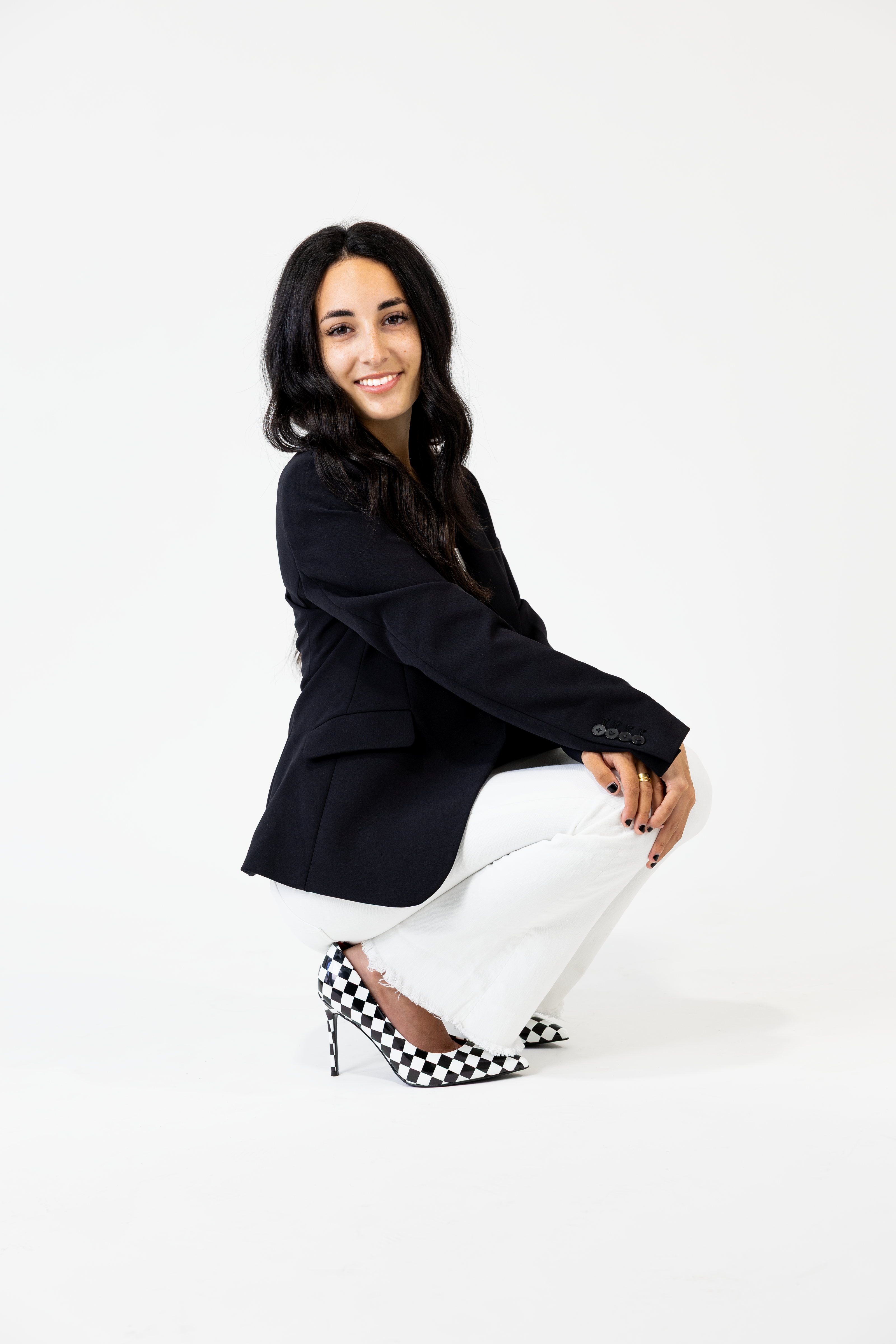Woman wearing a black blazer and white pants with checkered shoes on a white background