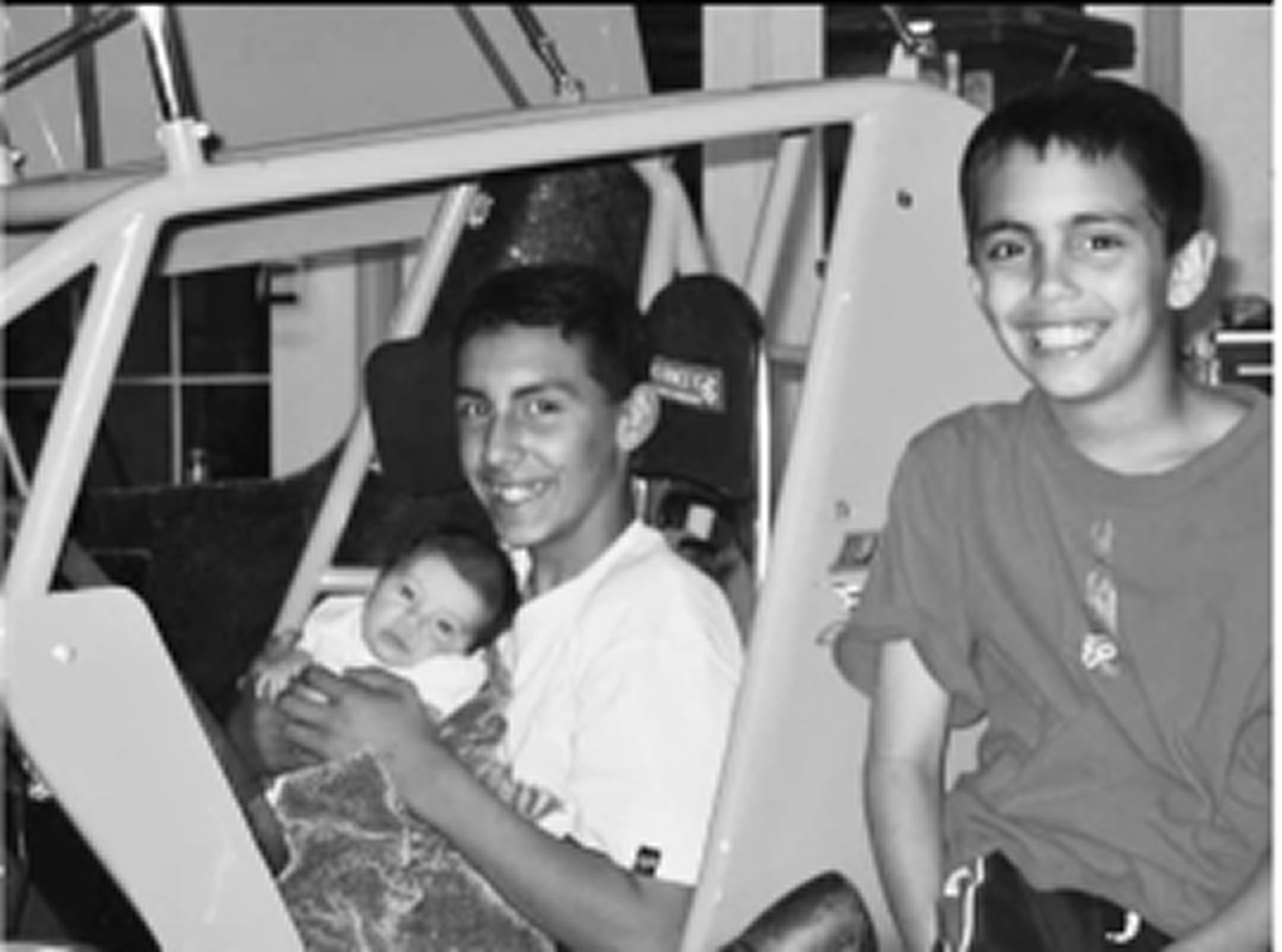 Two men sitting inside a vehicle with a baby, smiling.