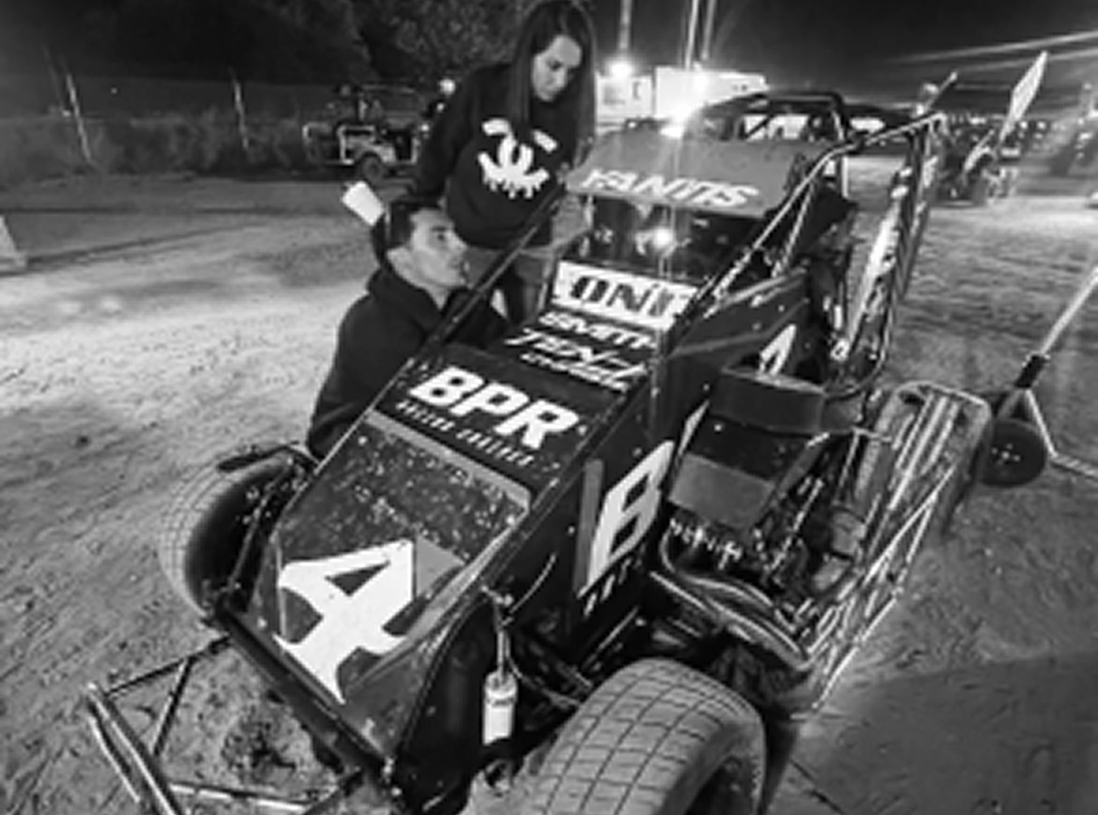 Person sitting in a race car with sponsor logos at night